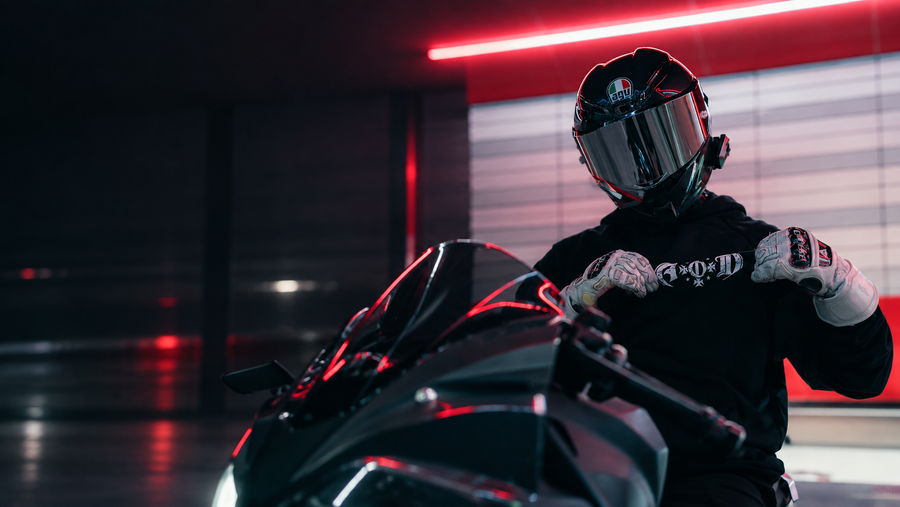Helmeted Adapt or Die rider in a black hoodie and white gloves beside a black sport motorcycle under red light, Los Angeles