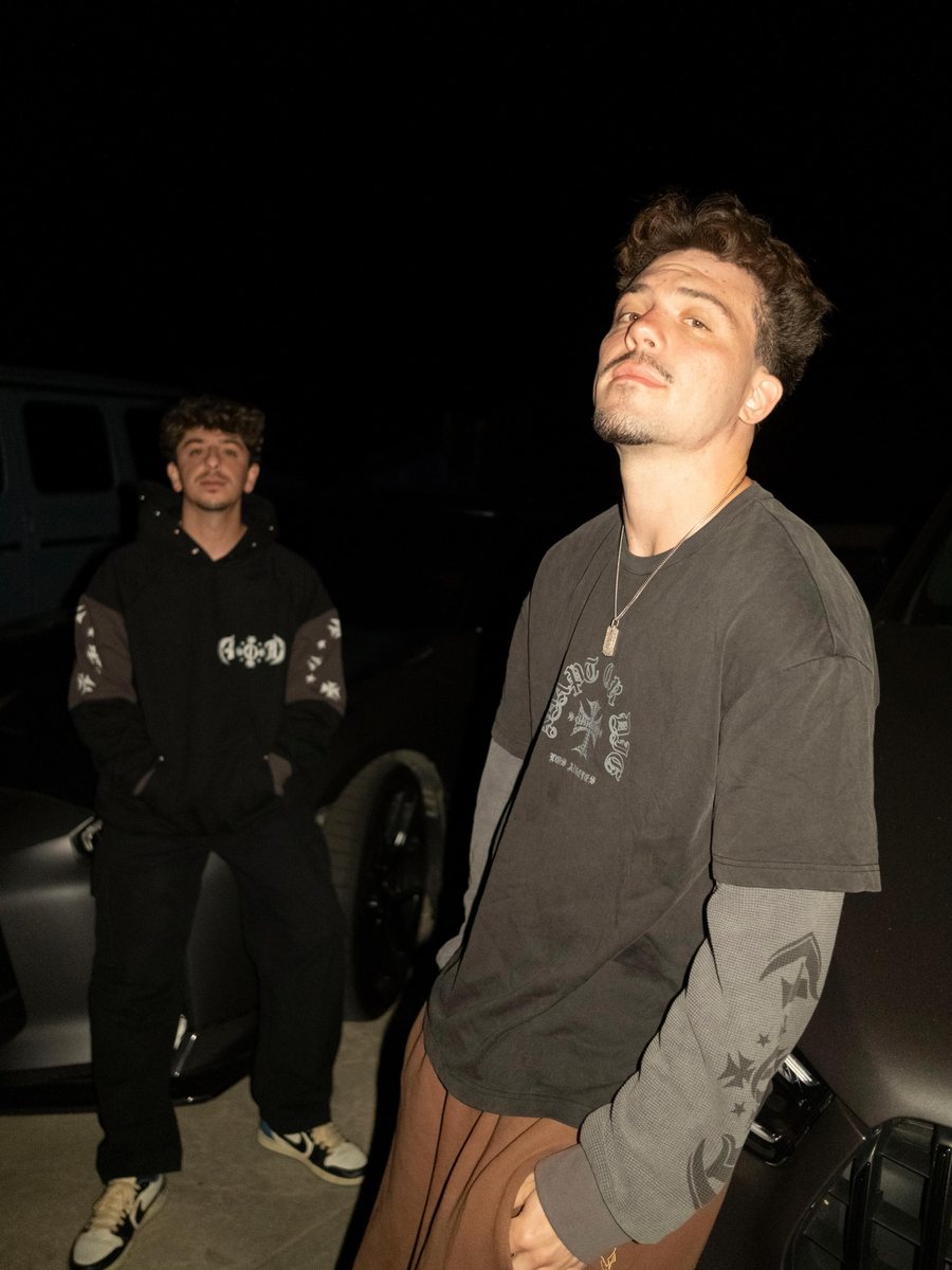 Two figures beside a car at night wearing Adapt or Die